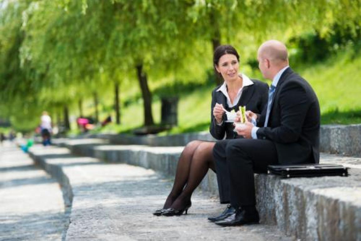 two people eating lunch together sitting on a concrete wall outside