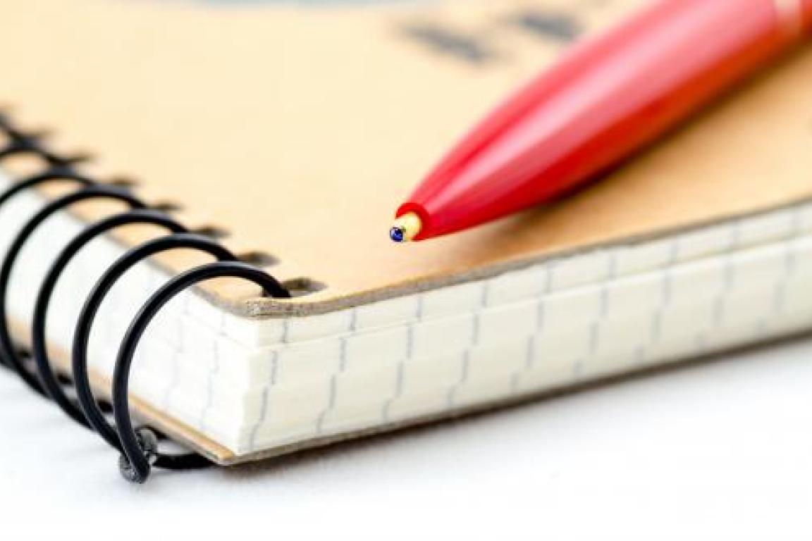 A spiral notebook with a red pen on top of it