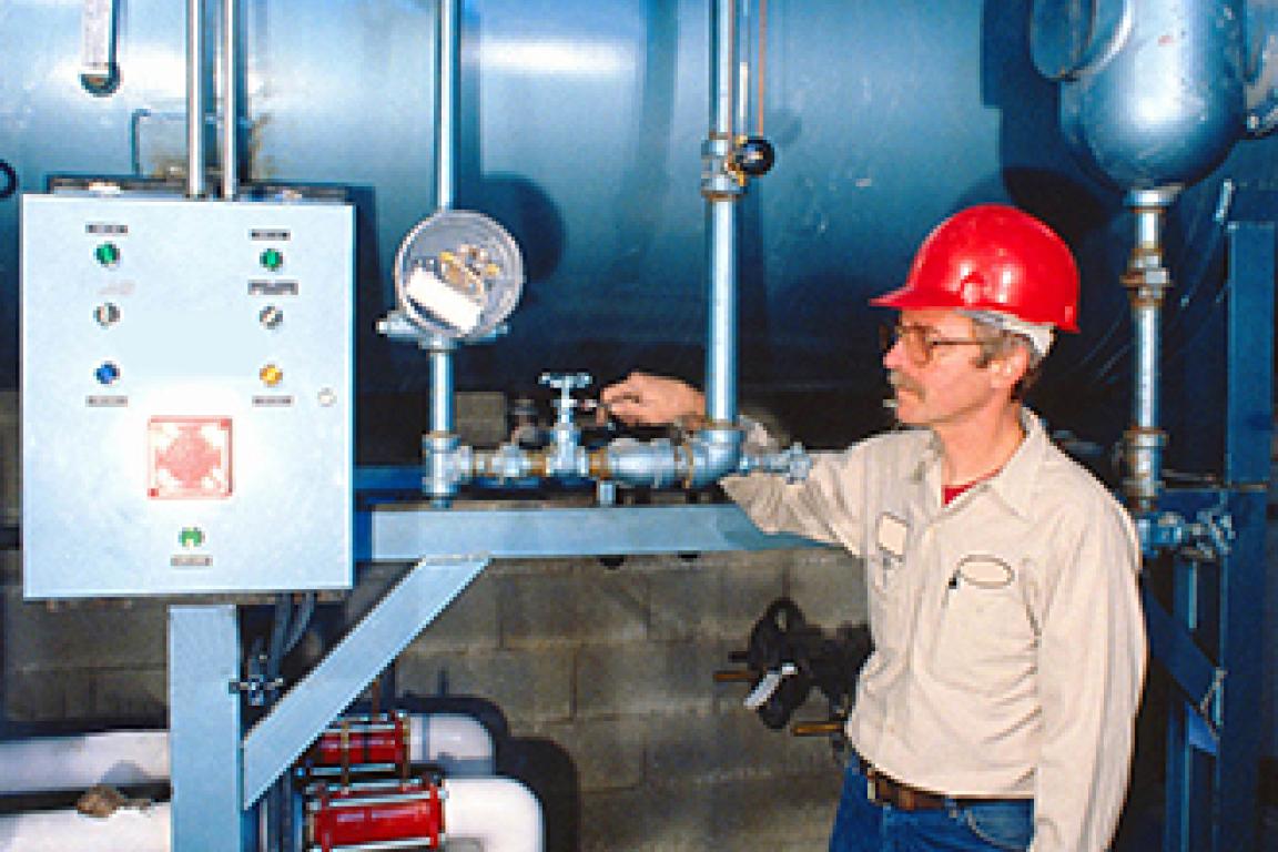 A person in a red hardhat works on a pressure vessel