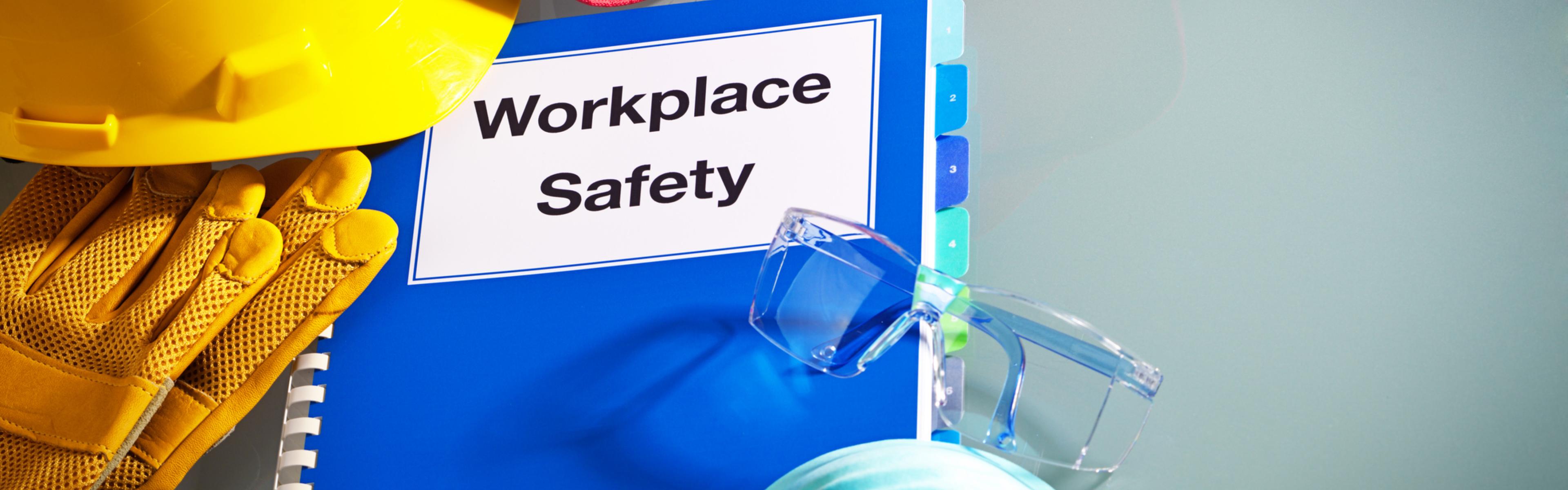 A blue notebook says "workplace safety" surrounded by a first aid kid, a respiratory mask and a hard hat. 
